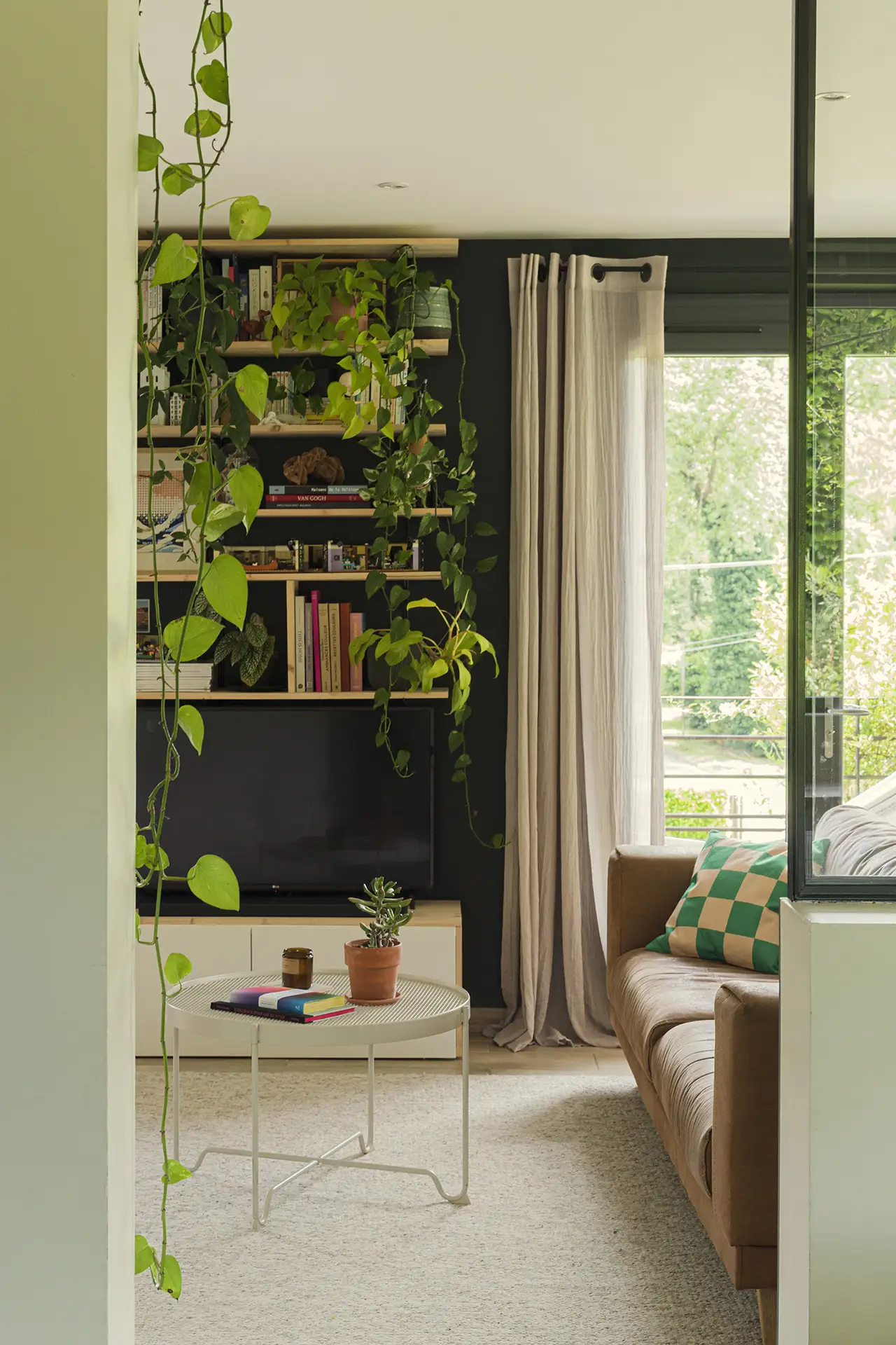 Photo d'un salon cosy au style franc avec ses murs vert sombre mettant en valeur la végétation luxuriante du jardin et des plante intérieures.