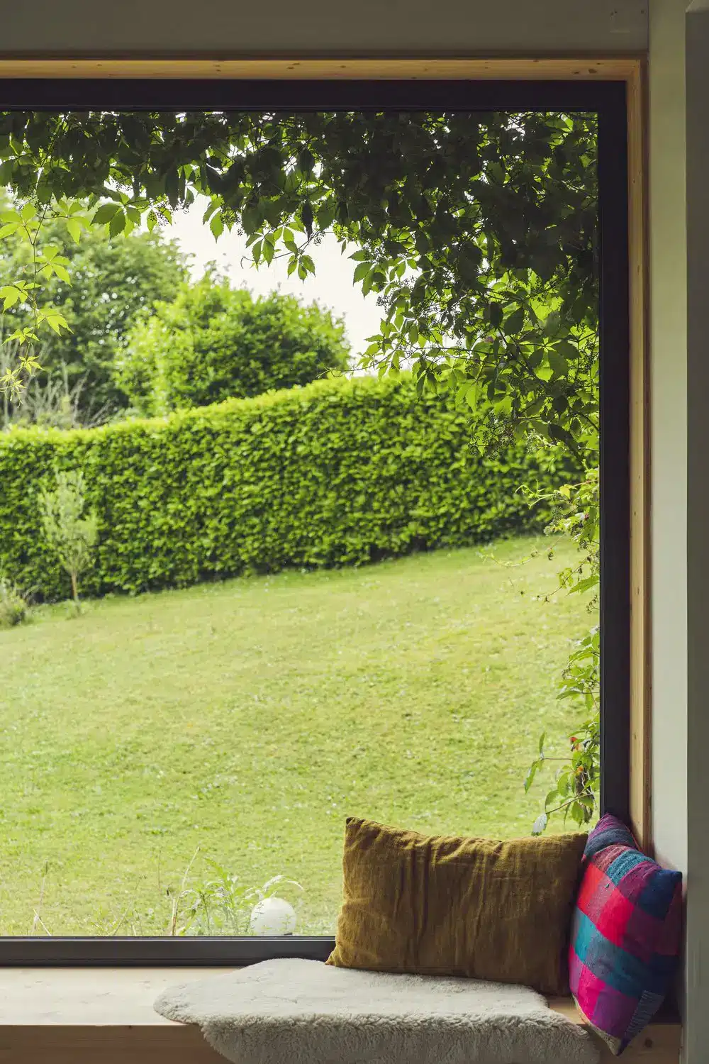 Photo d'une banquette en bois sur mesure devant une grande fenêtre fixe ouvrant sur un jardin luxuriant.