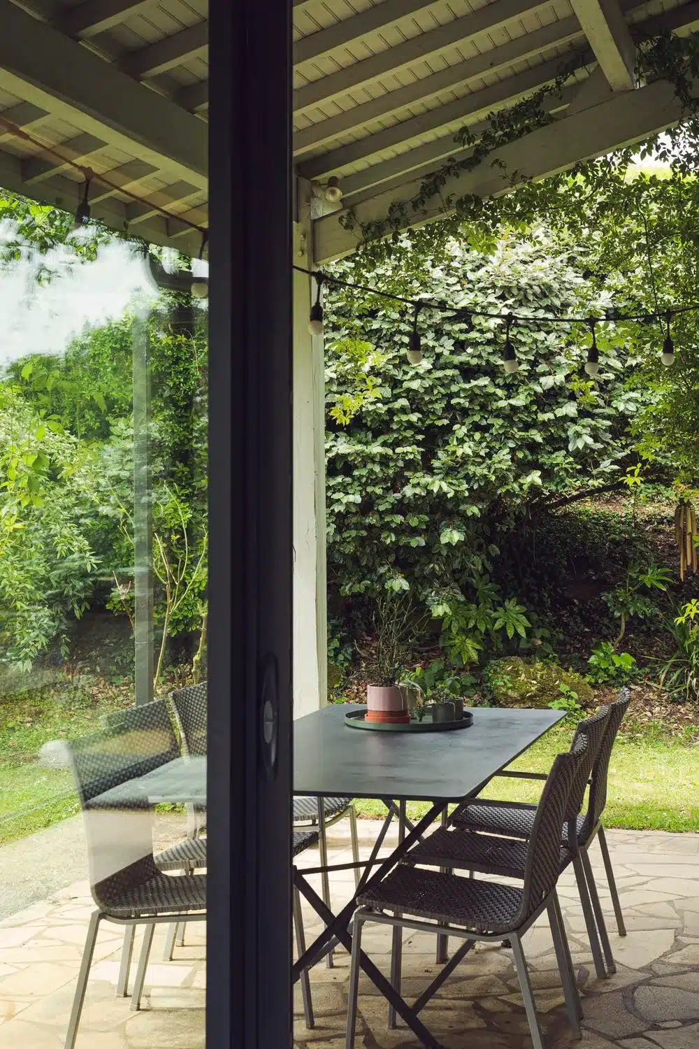 Photo d'une terrasse entourée de nature avec son mobilier en métal gris anthracite qui fait ressortir le vert de la nature environnante.