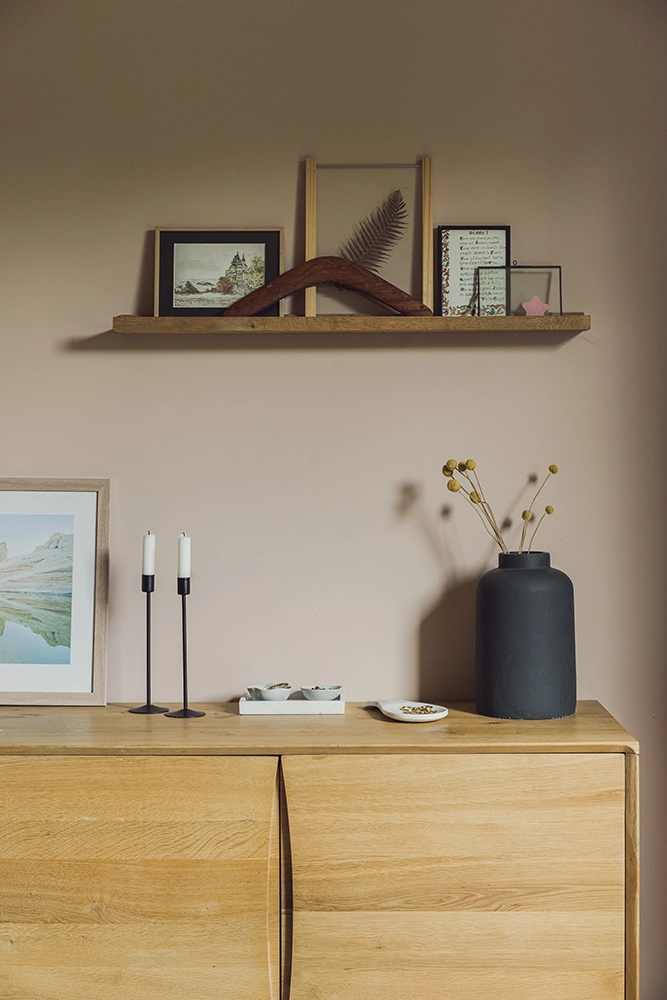 Photo d'étagères en ois contre un mur vert foncé avec beaucoup de caractère. les touches de couleurs du tableau peint à la main et de la petite lampe orange vibrent et l'oeil est attiré vers l'extérieur en second plan.