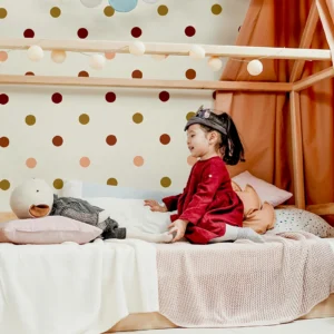 Papier peint à pois terracotta, ocre et rose sur fond blanc cassé, parfait pour une chambre d'enfant avec de la joie sans trop alourdir les murs.